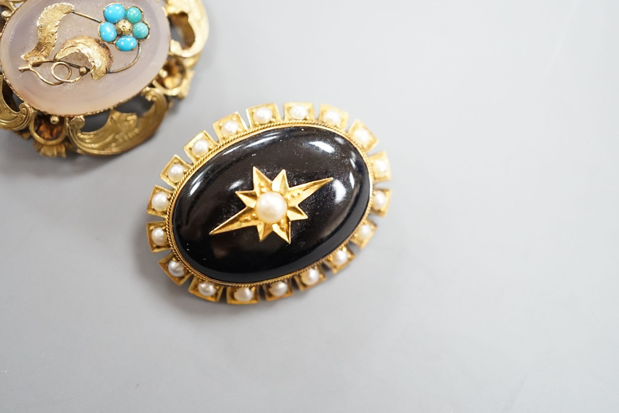 Two Victorian yellow metal and gem set oval brooches, including black enamel and split pearl, largest 34mm.